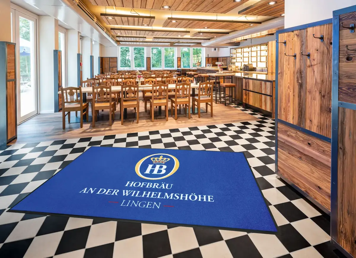 Blaue Logomatte mit Hofbräu-Logo im Eingangsbereich des Restaurants an der Wilhelmshöhe in Lingen